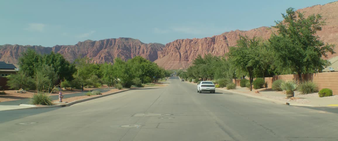 A white sports car driving on a suburban road by a rocky canyon