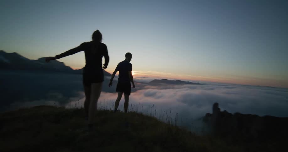 Two people running on top of a mountain at sundown