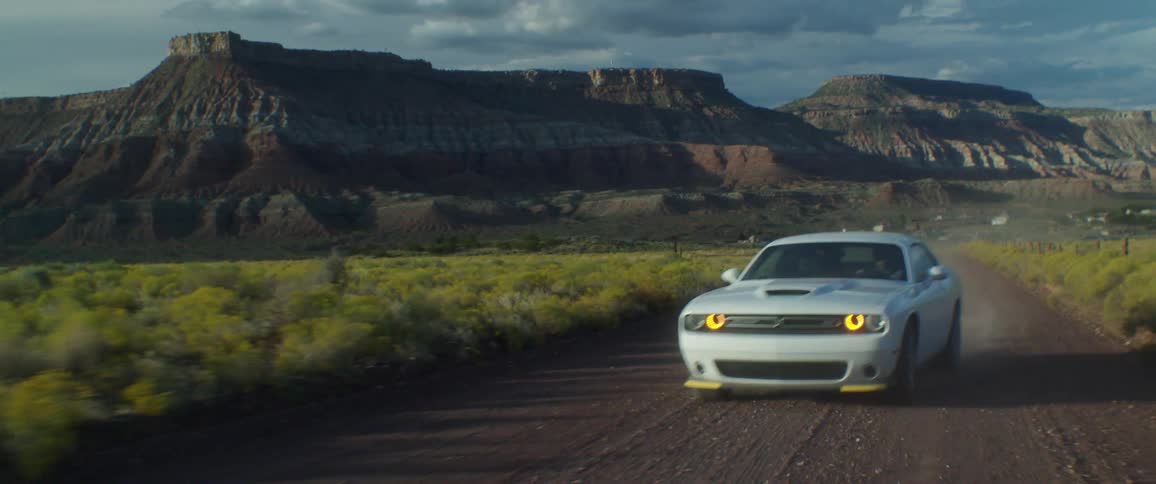 A white sports car driving on a dirt road in a region with mountains in the background