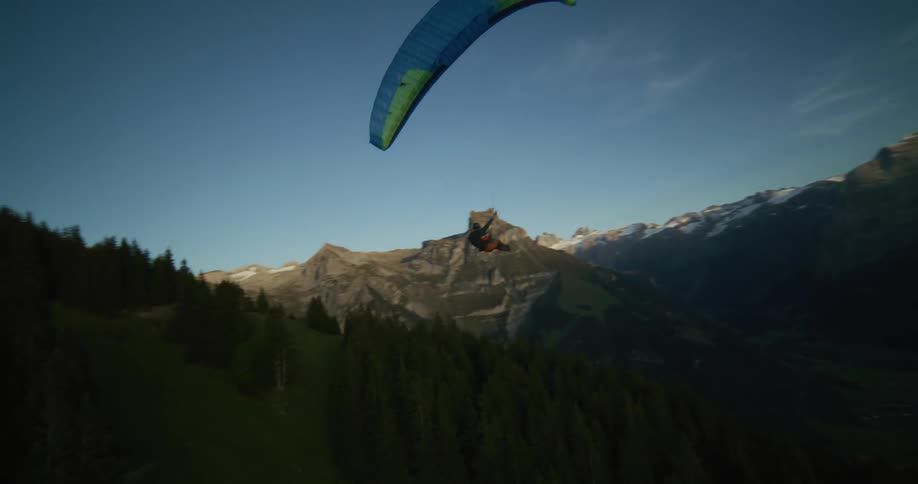 Aerial view of a man paragliding gracefully over a green forest on a mountain slope