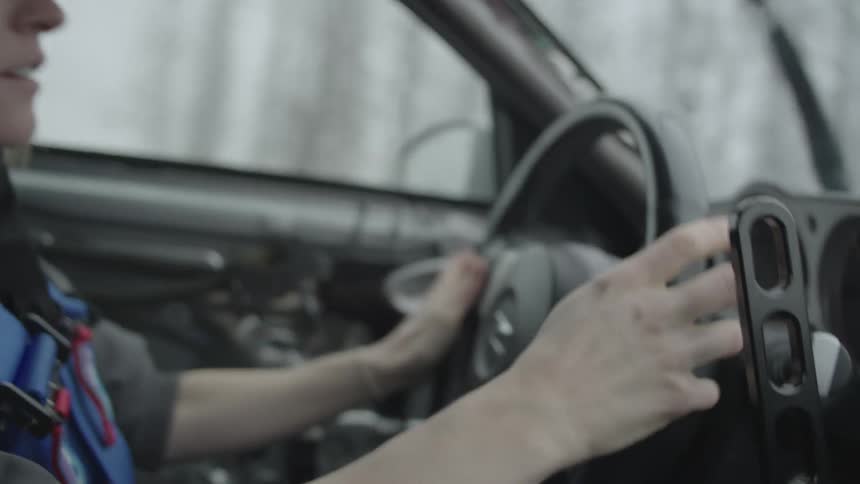 Woman steers and shifts while driving past woods