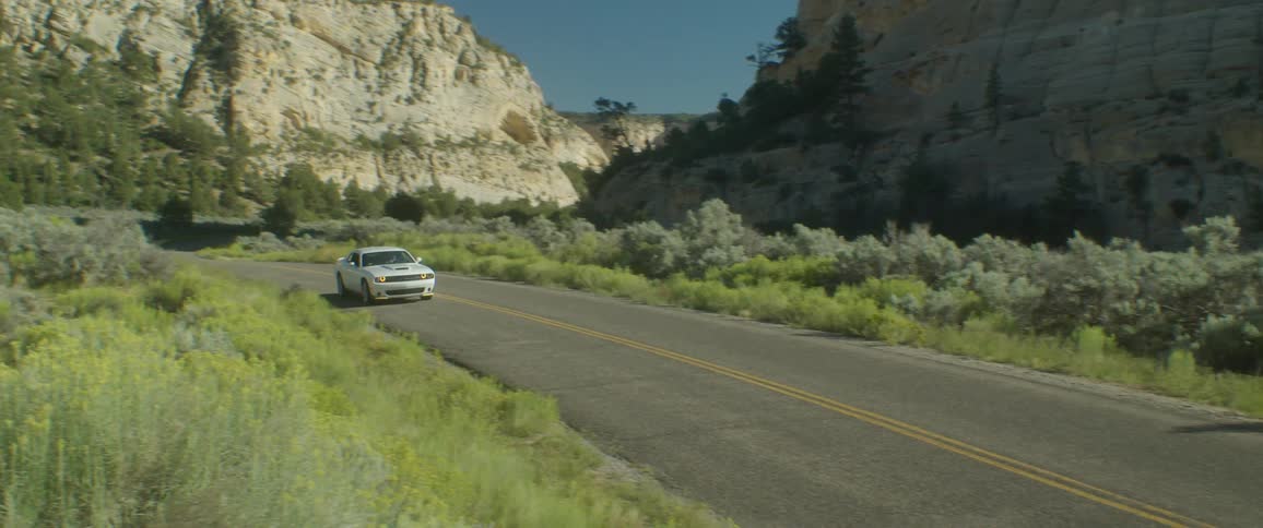 A white sports car travels on a road curving around mountains