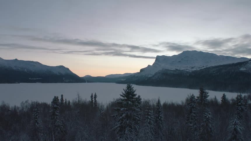 A hint of pink sunrise can be seen between mountains near a frozen lake