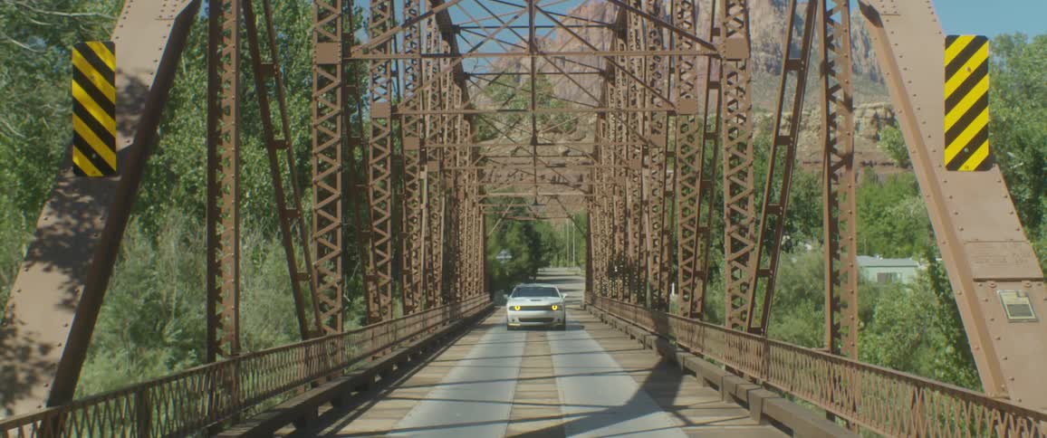 A white car travels across a bridge with a mountain in the distance