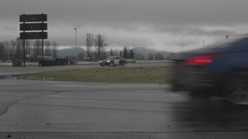 Sports cars race along wet race track with foggy mountains in the background on an overcast day