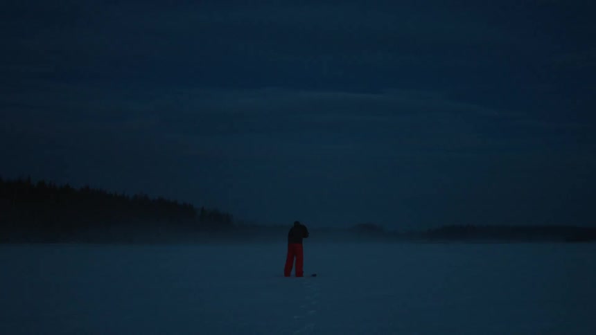 A man stands on a frozen lake working an ice auger