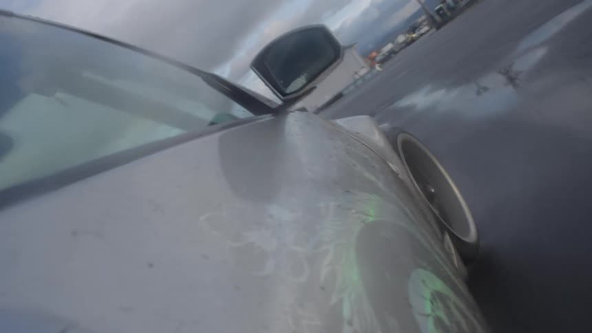Side passenger side tire profile of a white car racing on a round asphalt road with a blue car in front
