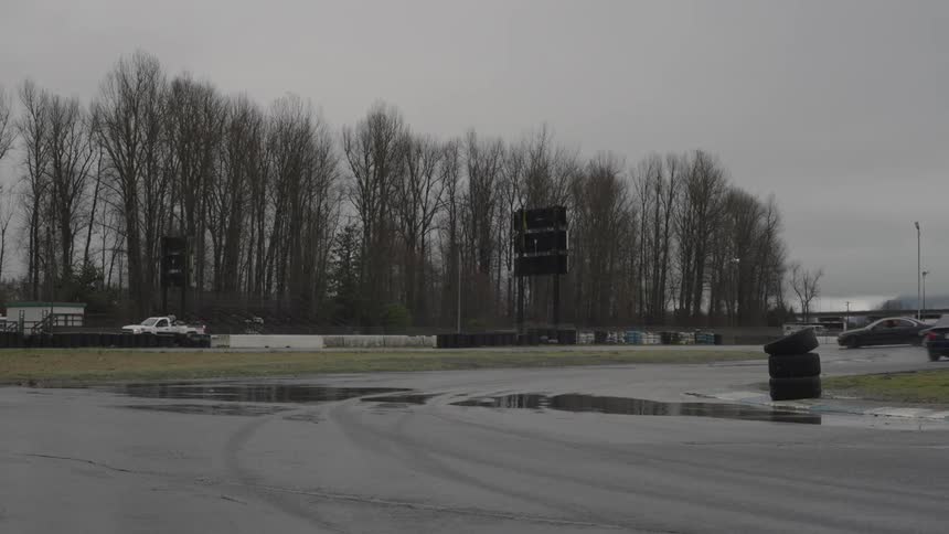 Some cars drifting on an asphalt track with puddles of water