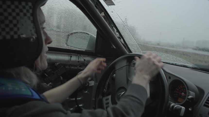 A woman in a helmet driving a car and turning the steering wheel quickly while it rains