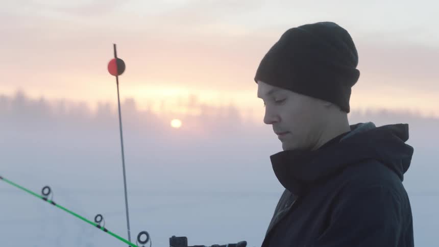 An ice fisherman adjusts his fishing pole