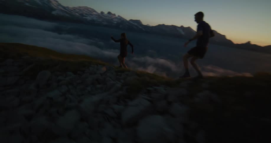Two people are running on top of a mountain on a dark morning with the sun rising