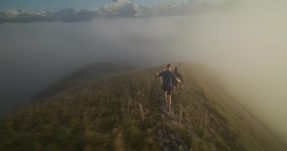 Two people running on top of a hill above a fog