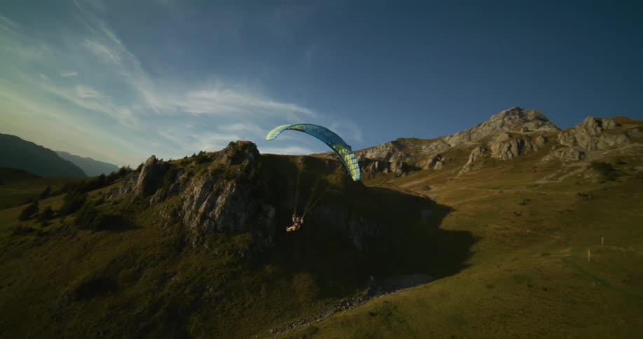 A man flying a paraglider floats along the side of a mountain cliff