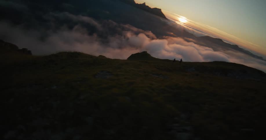 An aerial view of a mountain near a fog and on the horizon the sun is shining