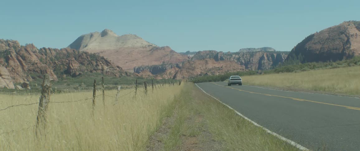 A white car driving on a country road with some mountains on the side