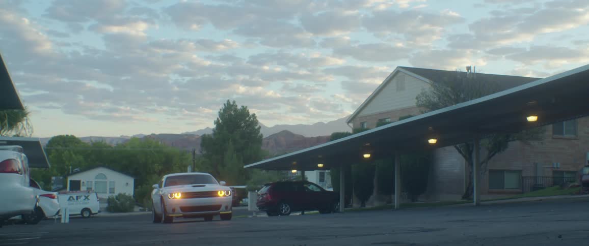 White dodge challenger pulls into a residential apartment carport parking driveway in the evening