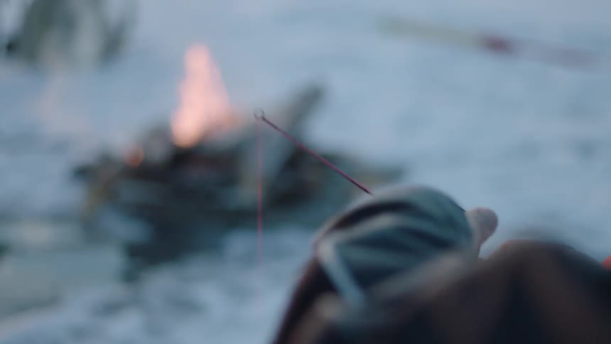 An ice fisherman reels in while a campfire burns