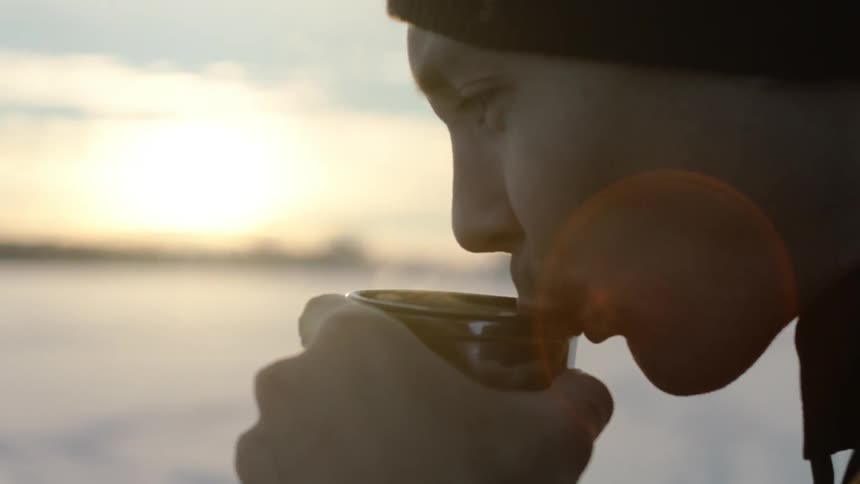 A man sips steaming liquid out of a mug outside in winter