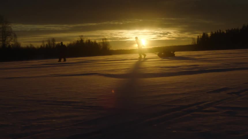 Two people walk across snow covered ground at sunset