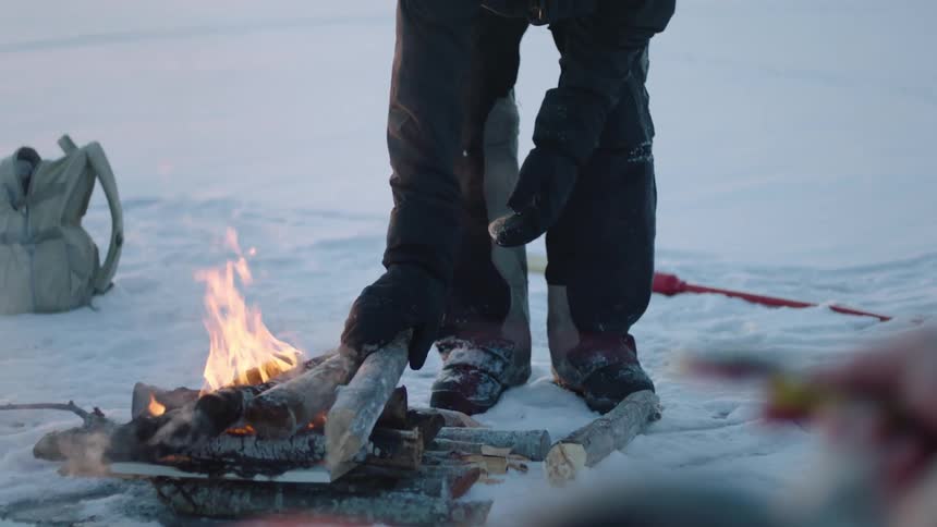 One ice fisherman tends a fire while the other fishes