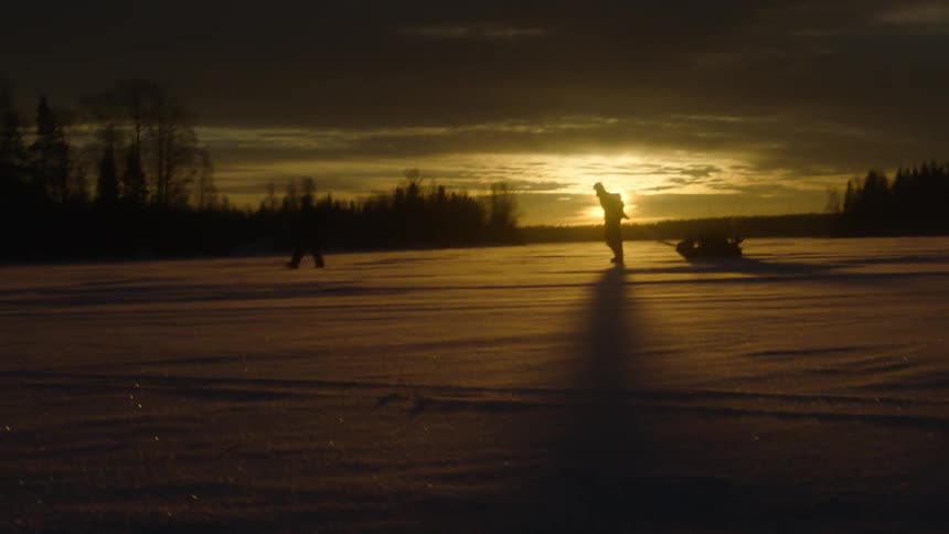 Two people walk across a frozen lake as the sun sets