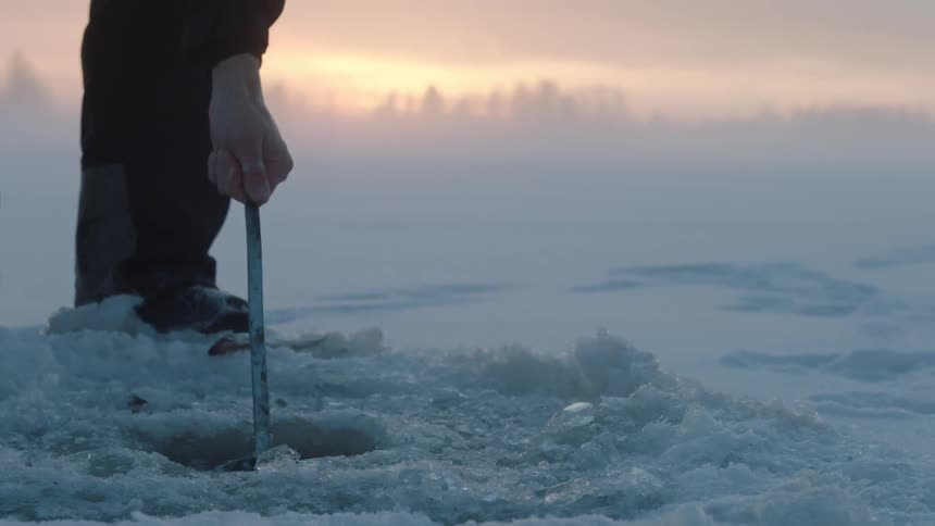 A man uses a tool to scoop ice out of an ice fishing hole