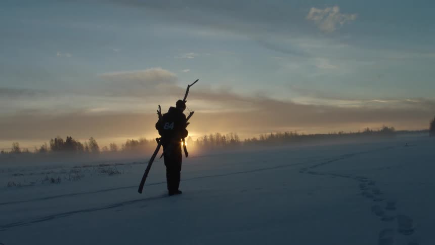A person carries long sticks in the snow at dusk