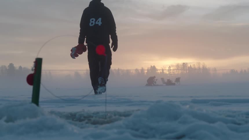 A man carrying an ice auger walks away from a fishing hole he's set up