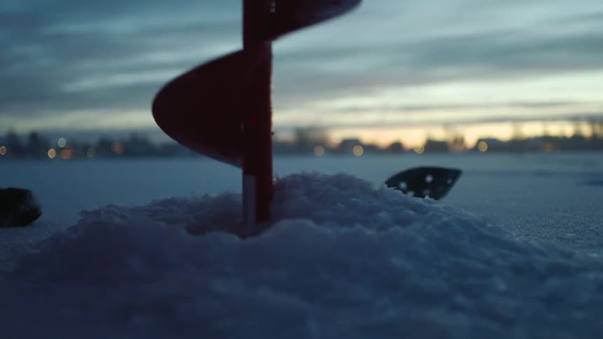 A hole is drilled into a snow and ice-covered lake