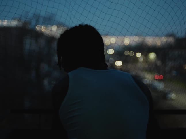 Silhouette of a young, black man looking at a city through a net