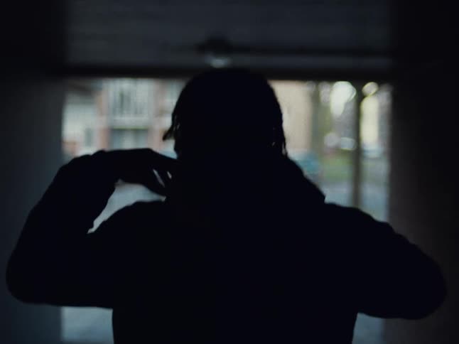 A young black man puts on a hoodie as he walks out into the street