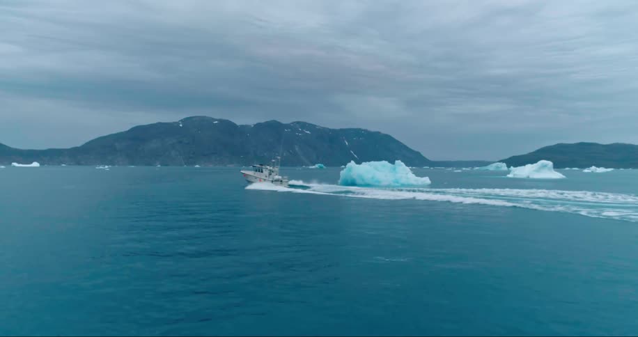 Boat goes past icebergs in the ocean under a cloudy sky