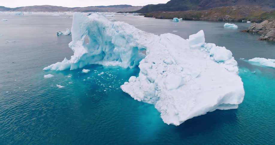 A large iceberg sits in the middle of a lake surrounded by mountains