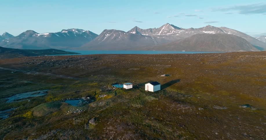Two lone houses in a grassy plain with a mountain range as backdrop