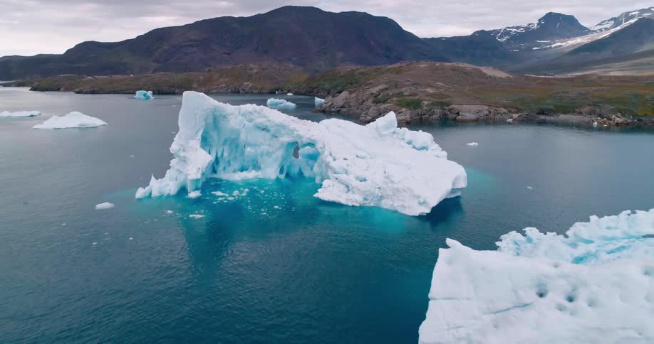 Melting icebergs float off the arctic coast with mountains in the distance