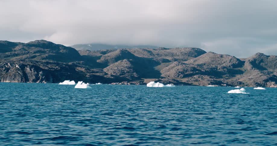 Large chunks of ice float at the surface of the ocean near a rocky coastline