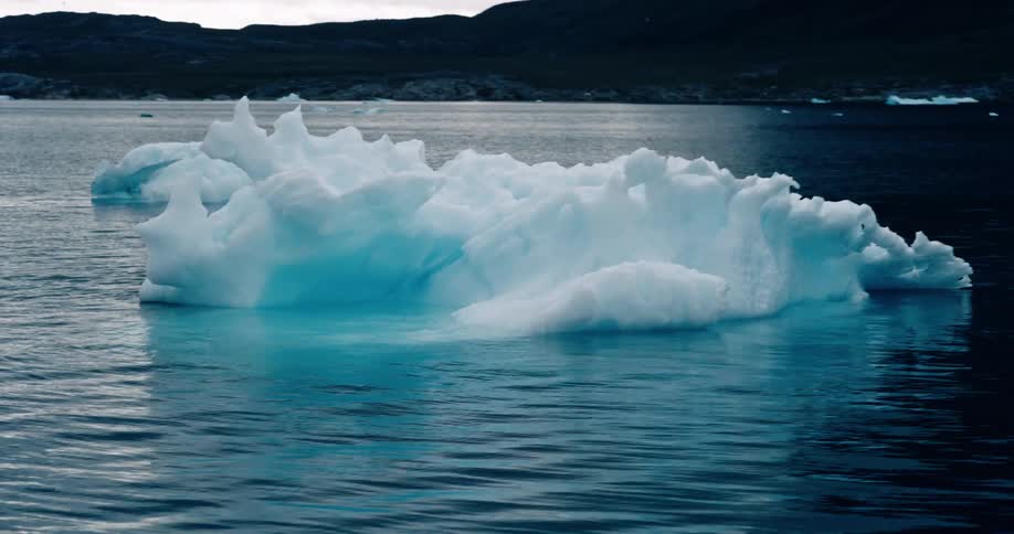 Ice chunks float in a lake beside low mountain hills