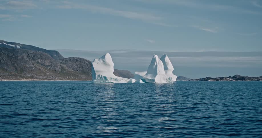 Two large icebergs are sitting in an ocean in front of a mountain