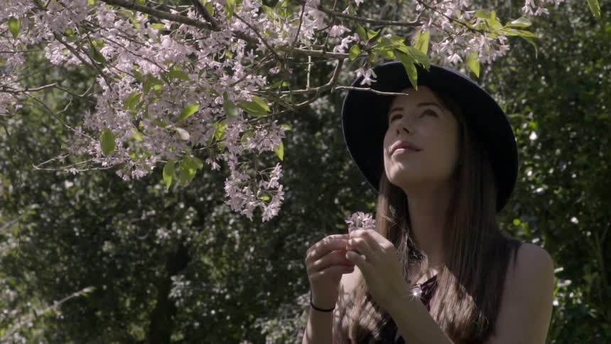 Young woman looks at a flowering tree holding a blossom