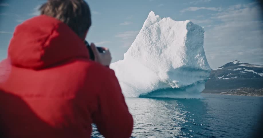 A man is taking a photo of an iceberg