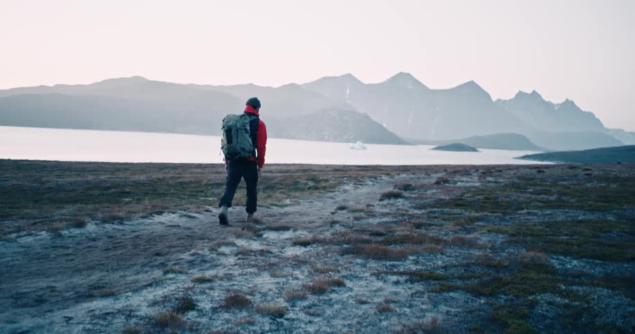 A man with a backpack walking in a coastal area at midday