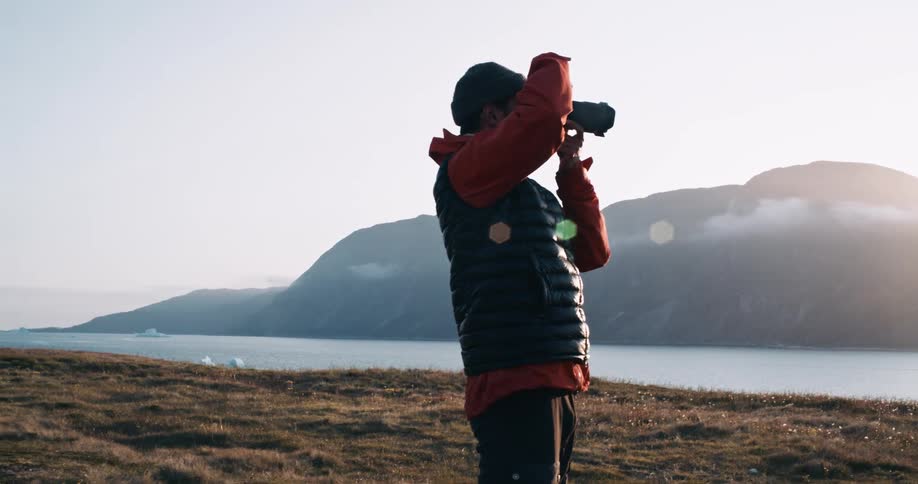 Man taking photos with a professional camera beside a lake with mountains