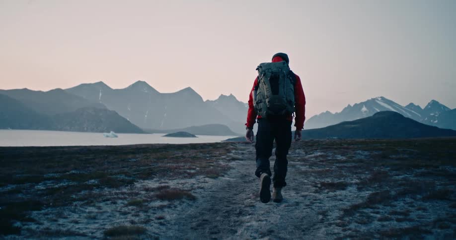 A hiker walking through a path covered in mud and snow near a body of water
