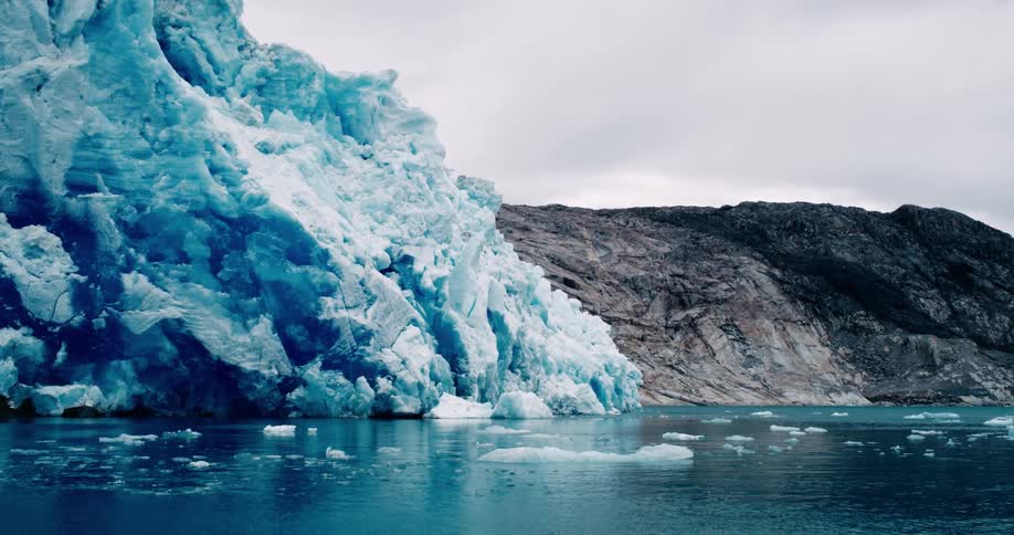 Ice glacier next to a sloped rock formation in icy blue water on a bright day