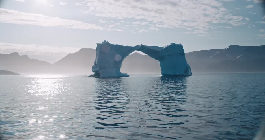 Man rides boat approaching ice arch floating off foggy coast on a cloudy day