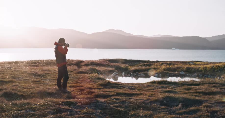 A man taking a photo of a small pond near a large lake
