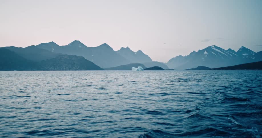 An ocean with small waves and mountains behind it against a blue sky