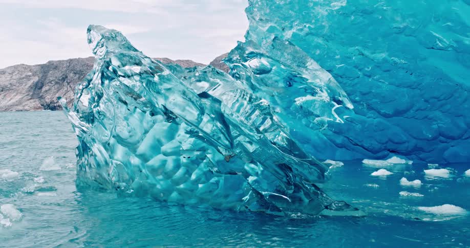 Iceberg of translucent blue ice floats offshore on a cloudy day