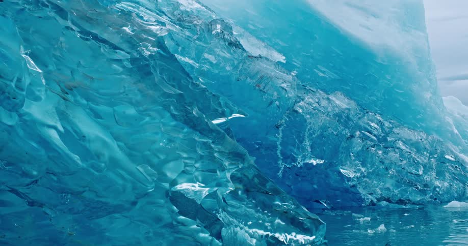 A blue translucent iceberg floating in the arctic ocean