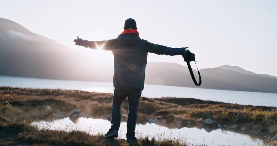 A happy man reaches out his arms by the mountains